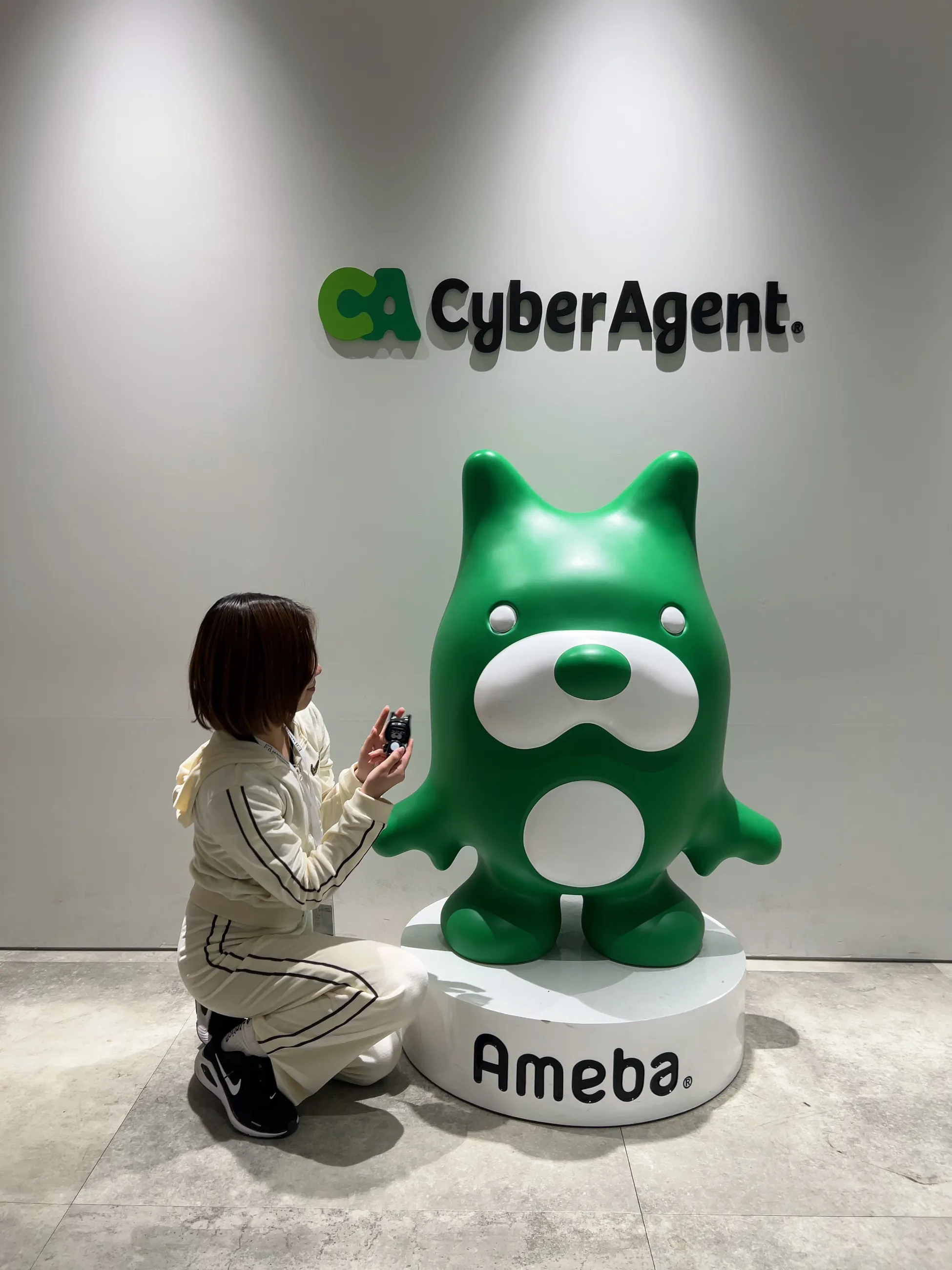 サイバーエージェントのオフィスで、アメーバくんの像の横にしゃがむ様子